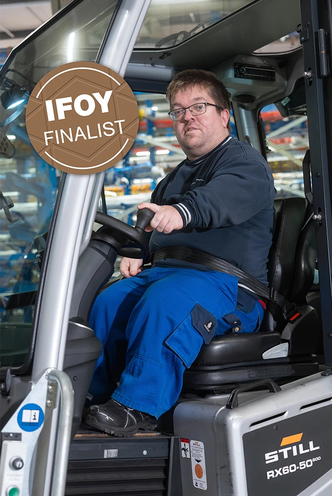 Ein angeschnallter Mann mit Brille sitzt am Steuer eines STILL RX60-50 Gabelstaplers, daneben das Siegel „IFOY Finalist“.