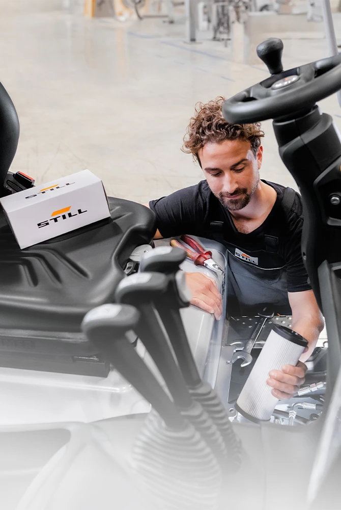Ein STILL-Servicetechniker hält bei der Wartung eines Gabelstaplers eine Filterpatrone in der Hand, auf dem Fahrersitz steht ein STILL-Ersatzteilkarton.