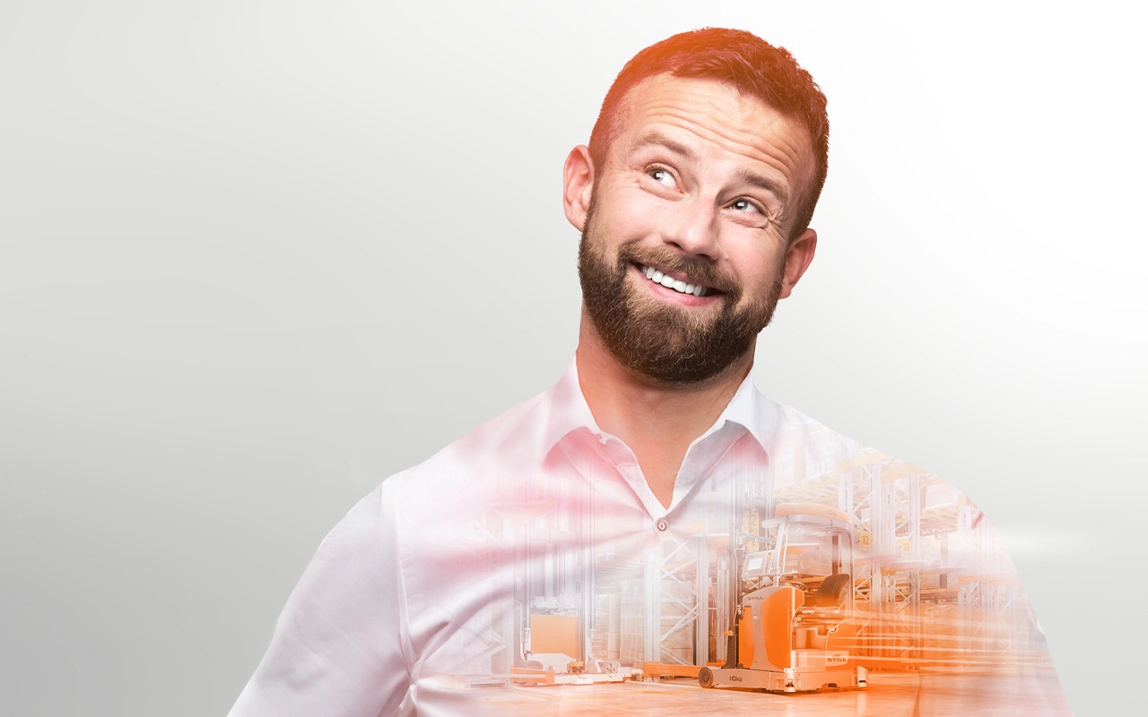 A smiling man in a white shirt looks thoughtfully upwards. A warehouse with orange automated industrial trucks is blended into his shirt.