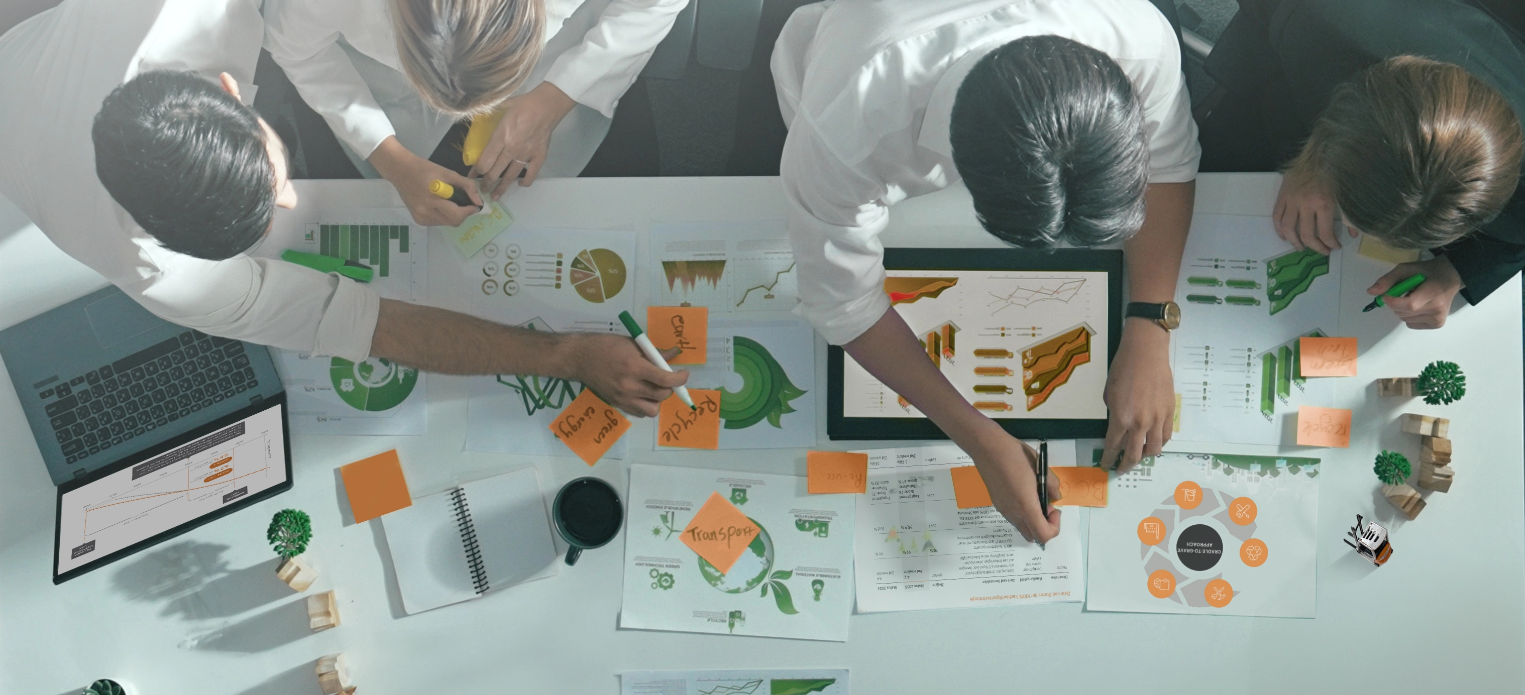 Top view of four people working at a table covered with sustainability charts, sticky notes and a laptop.