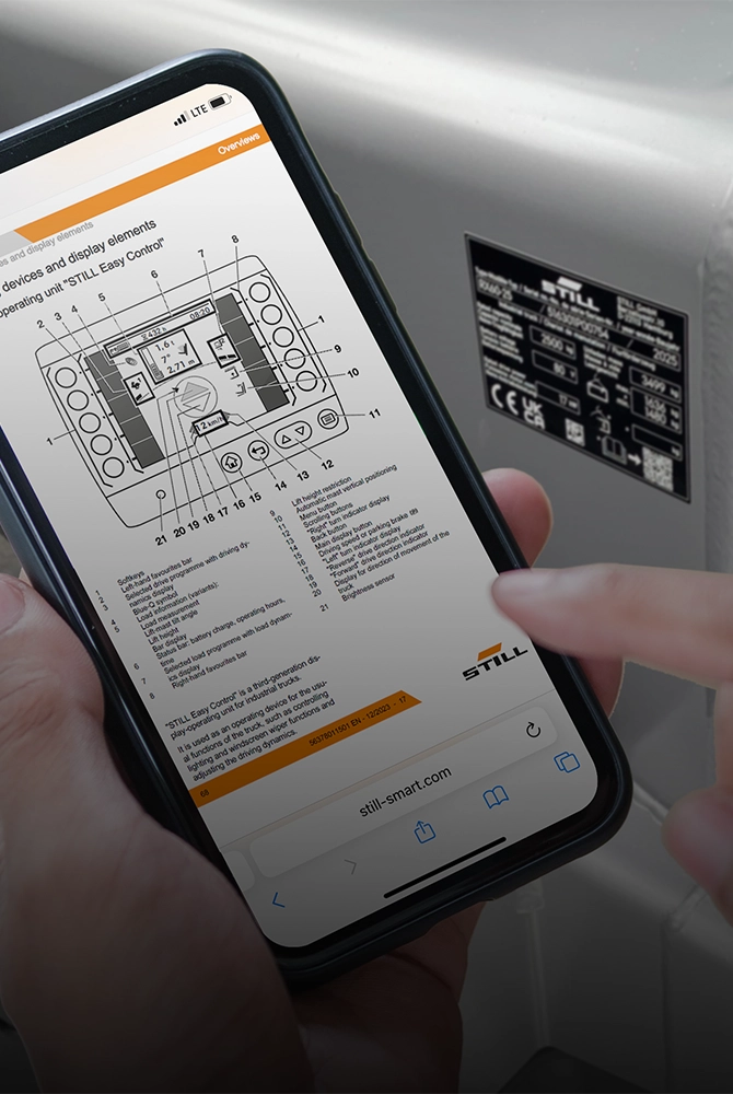 A hand holds a smartphone showing a digital document with a technical diagram, in front of an industrial truck.