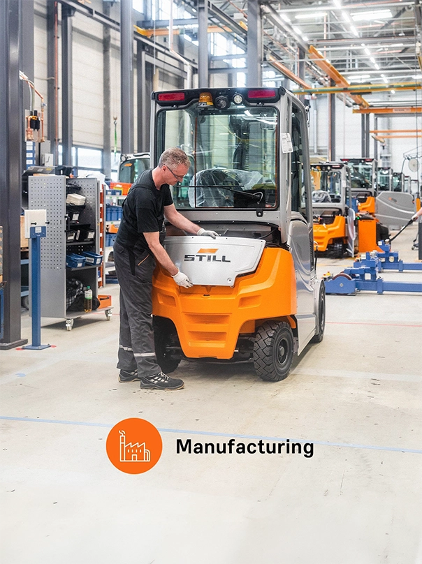 A worker fits a part to the rear of an orange and grey STILL forklift in a production hall, labelled “Manufacturing".